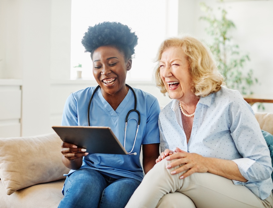 nurse caregiver showing a tablet screen to senior woman and laughing at home