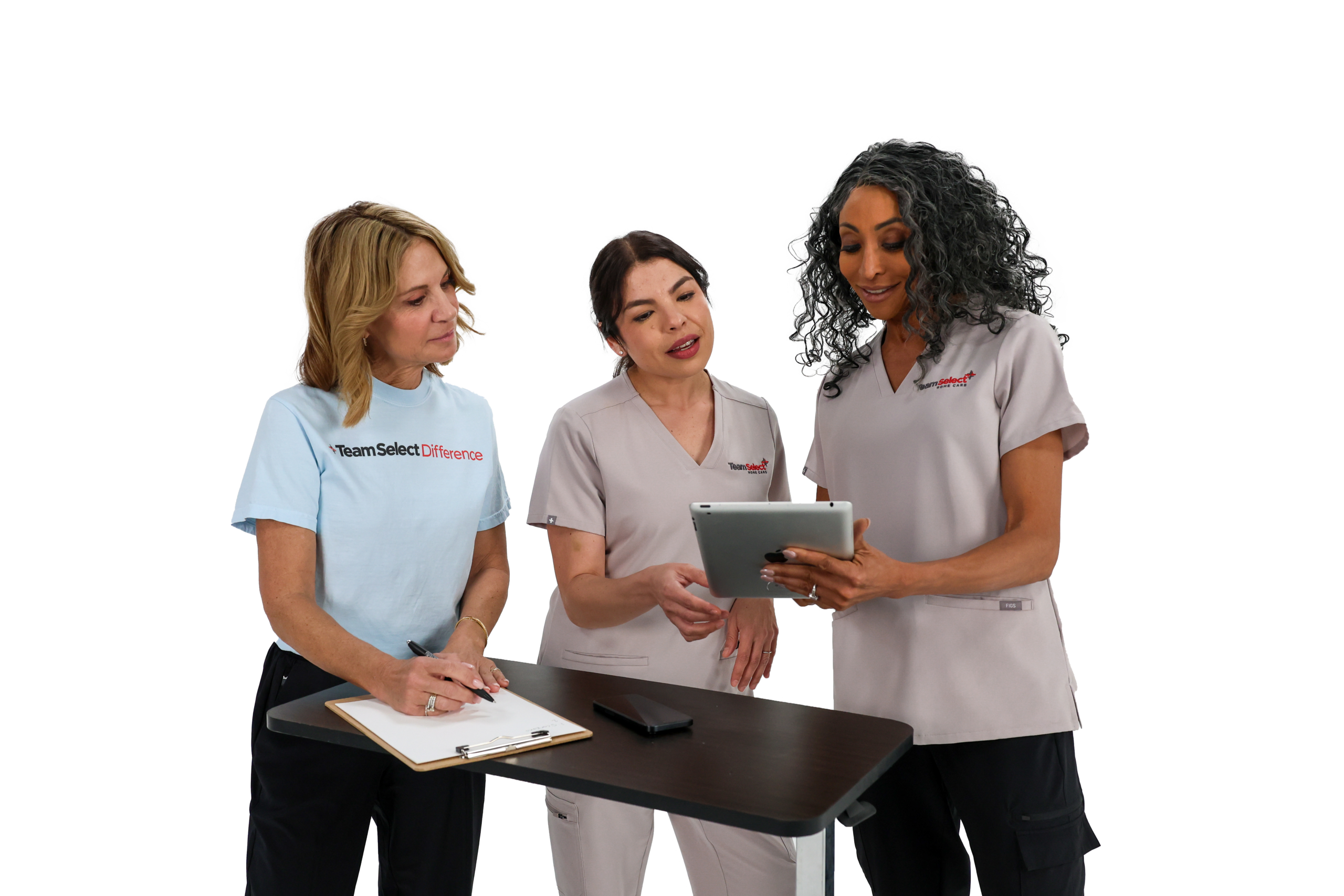 Three medical professionals stand around a table, reviewing documents and a tablet together.
